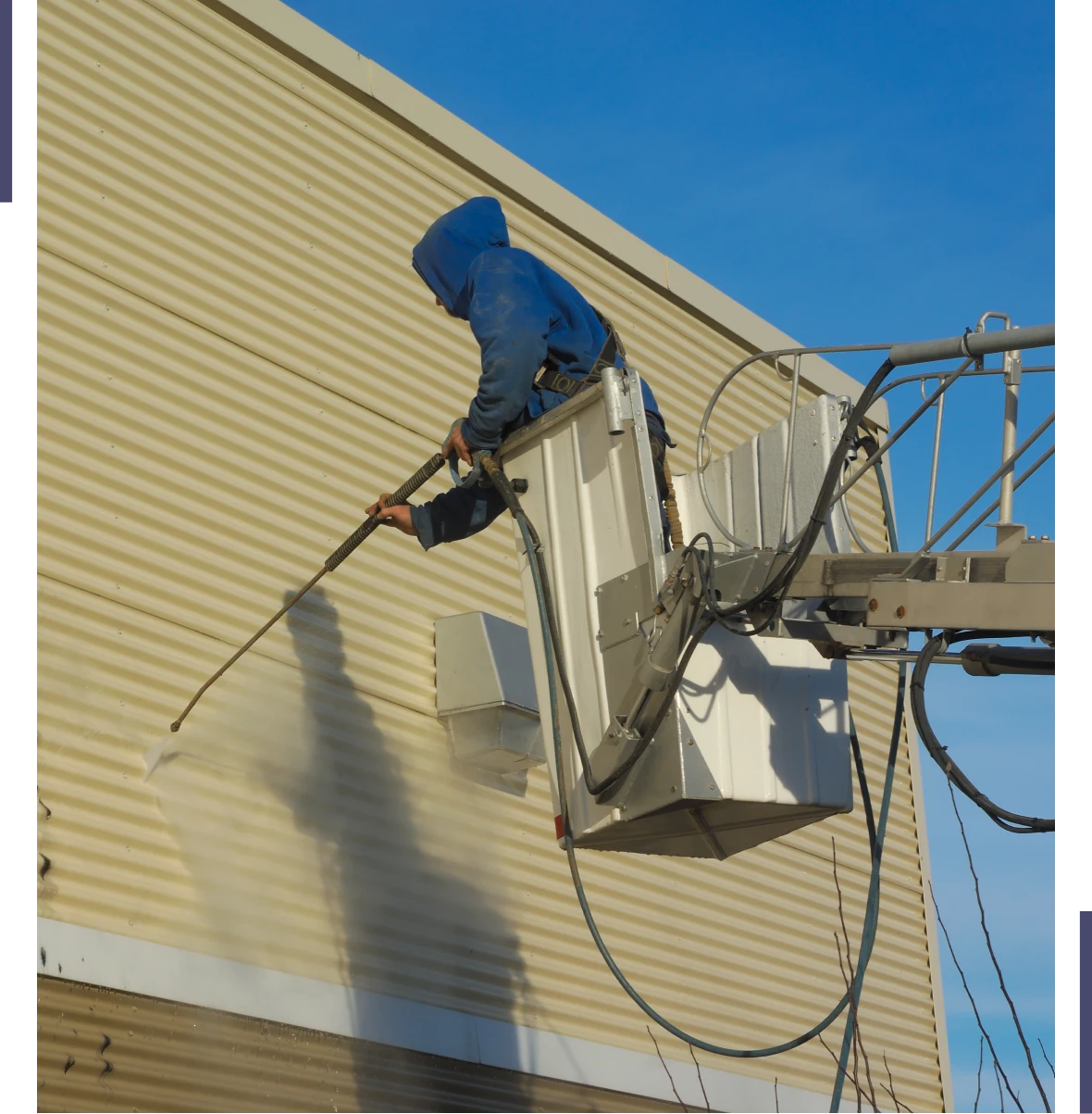 Worker pressure washing the side of a building from a lift.