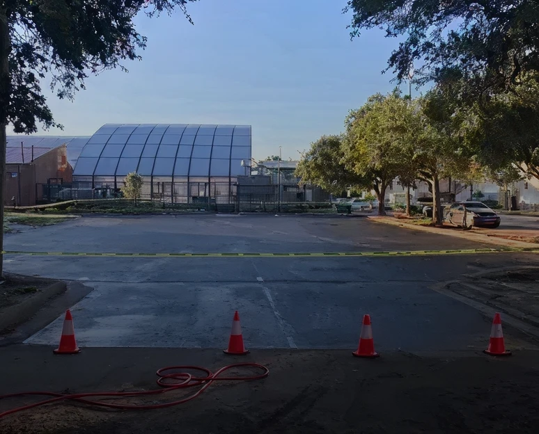 Empty parking lot with trees and a large building in the background.