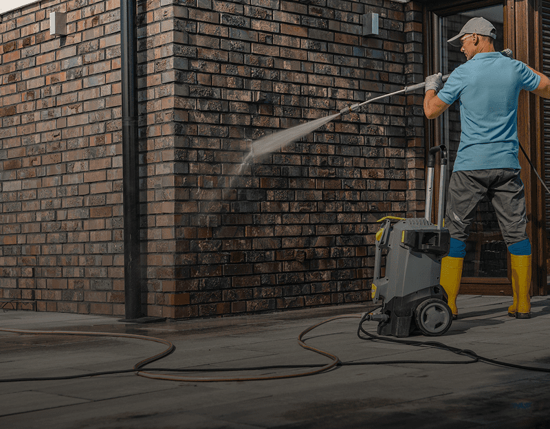 Man pressure washing a brick wall outdoors.